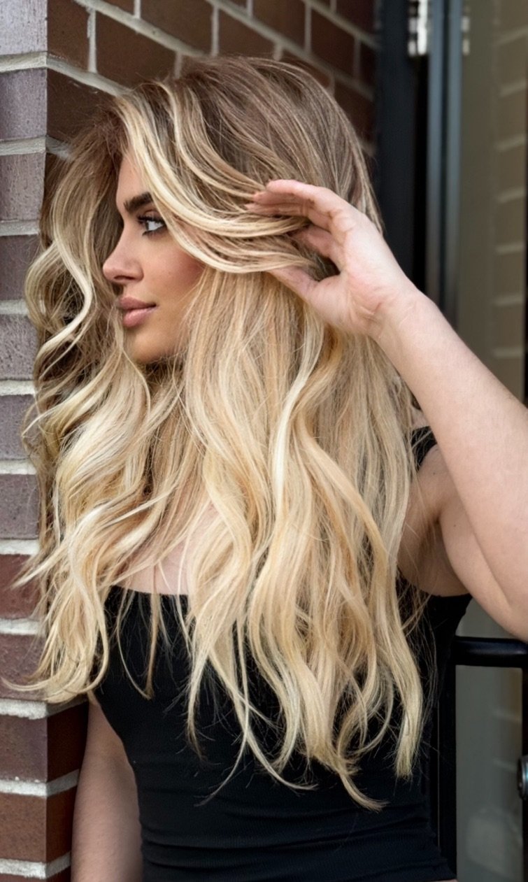 Long dimensional blonde hair styled in loose waves beside a brick wall